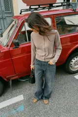 Chaqueta de punto color beige, de manga larga y corte corto, con cuello redondo y puños terminados en puntilla blanca a contraste.