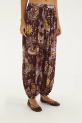 Pantalón babucha de tiro medio con cintura elastizada, silueta amplia y puños en los tobillos. Presenta un estampado ilustrado de inspiración artística sobre fondo bordó.