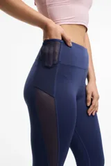 Calza deportiva larga color gris, con cintura alta, detalles de transparencias laterales en tul y bolsillos laterales.