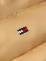 Chaleco acolchado color beige con capucha desmontable, cierre frontal con cremallera, dos bolsillos laterales con cremallera y logo de Tommy Hilfiger bordado en el pecho. Confeccionado en poliéster reciclado con acabado repelente al agua.