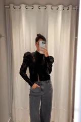 Camisa de encaje negro con cuello alto, mangas largas con hombreras abullonadas y diseño ajustado.