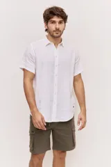 Camisa de manga corta en color blanco, con cuello clásico y cierre frontal de botones al tono. Presenta un diseño versátil de corte regular y textura liviana, ideal para looks frescos.