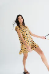 Vestido corto de algodón liviano, color amarillo con estampado floral en tonos oscuros, cartera de botones asimétrica y volado en el ruedo.