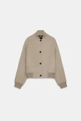 Cazadora bomber beige confeccionada en hilatura con lana, con cuello subido, manga larga y bolsillos frontales. Presenta cierre frontal con botones oscuros y puños, cuello y ruedo en tejido rib.