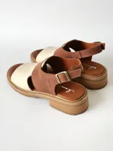 Sandalias de cuero combinadas en color marrón y crudo, con suela track y taco bajo. Tienen tira ajustable con hebilla en el talón.