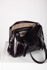 Cartera tipo bolso de mano y hombro de cuero color bordó, con diseño estructurado, doble asa corta y detalles de correas con hebillas metálicas en el frente.