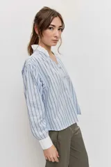 Camisa de rayas celestes y marrones, de corte holgado y manga larga, con cuello en V y detalles blancos en el cuello y los puños.