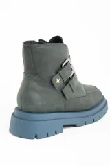 Bota corta de cuero color verde oscuro, con suela track gruesa de color celeste. Presenta dos correas ajustables con hebillas metálicas plateadas y un pequeño dije de estrella dorada en el lateral. Tiene cierre de cremallera en el interior.