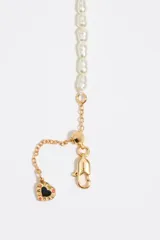 Collar de perlas sintéticas con delicados dijes colgantes de cadenas metálicas doradas. Cuenta con cierre de mosquetón y cadena de alargue con pequeño dije con detalle esmaltado.