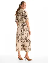 Vestido maxi de crepe color beige con estampado floral en tonos marrones y negros. Presenta cuello a la base, escote en V, abertura central con botones y cintura con lazo de ajuste y hebilla.