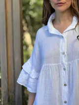 Vestido camisero blanco de lino italiano, con cuello camisero, cierre frontal con botones, mangas cortas con doble volado y bolsillos laterales.
