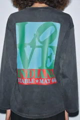 Camiseta de manga larga, corte regular, color negro con efecto lavado o acid wash. Presenta un estampado frontal en rojo con la palabra "LOVE" estilizada.