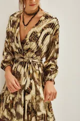 Vestido corto de estilo wrap con estampado abstracto en tonos dorados y marrones con acabado metalizado. Presenta escote en V cruzado, mangas largas con puños elásticos, lazo ajustable en la cintura y falda con volado en el ruedo.