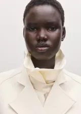 Chaqueta de mezcla de lana y poliéster color marfil, con solapas de muesca, cuello alto drapeado superpuesto y cierre cruzado con lazo ajustable del mismo tejido en la cintura.