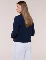 Camperita liviana de corte recto y acabado crepé color blanco, con cuello camisero clásico y cierre frontal de botones metálicos dorados. Presenta bolsillos en el pecho con solapa y mangas largas con puños abotonados.