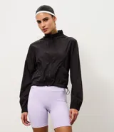 Campera rompevientos deportiva de corte cropped color negro, con capucha y cierre frontal por cremallera. Cuenta con mangas largas con puños elásticos y bajo ajustable por cordón.
