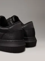 Zapatillas urbanas de cuero granulado color negro, con suela cupsole gruesa, interior de espuma, forro de malla de poliéster y logo de Calvin Klein en la lengüeta y el talón.