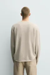 Jersey de punto de corte relajado, con cuello redondo amplio y mangas largas. Presenta un diseño de rayas horizontales finas en contraste sobre fondo beige.
