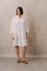 Camisola blanca de silueta amplia y caída liviana, con diseño clásico de cuello camisero, cierre frontal con botones y mangas tres cuartos, decorada con grandes motivos florales bordados.
