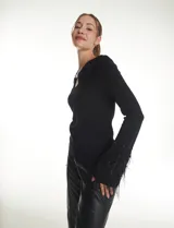 Blusa de punto negra con escote en V y detalle metálico en el pecho. Presenta mangas largas con puños decorados con apliques de strass y plumas negras.