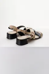 Sandalia de tacón bajo color beige con tiras cruzadas en el empeine y cierre de hebilla en el tobillo. La suela es negra.