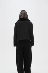 Chaqueta negra de corte holgado con cierre frontal, cuello camisero con detalle de corderito y bolsillos frontales con solapa y botones.