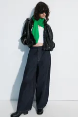 Chaqueta de cuero sintético negro con cuello alto, cierre frontal de cremallera oculto por solapa con botones a presión, mangas largas y bolsillos laterales. Diseño con volumen y bajo elástico.
