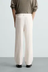 Pantalón de vestir color blanco hueso, de corte recto y tiro medio, con cintura elástica y cierre frontal de botón y cremallera. Presenta bolsillos frontales y bolsillos traseros de vivo.