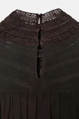 Blusa de cuello subido y manga larga, color marrón oscuro, con detalles de bordados combinados a tono en el canesú y los puños anchos. Cierre en la espalda con abertura y botones.