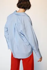 Camisa de manga larga en color celeste con estampado de rayas finas, cuello solapa y escote en pico con detalle de solapa frontal. Presenta puños abotonados y bajo asimétrico.