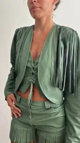 Campera corta verde con flecos negros en la parte superior y cierre frontal con lazo.