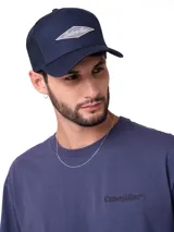 Gorro trucker azul marino de siete paneles, con visera curvada y parte trasera de malla transpirable. Cuenta con un parche bordado en rombo con el logotipo de Caterpillar en el frente y cierre ajustable a presión en la parte posterior.