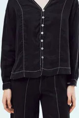Camisa negra de manga larga con cuello en V, cierre frontal de botones y costuras decorativas en contraste de color blanco.