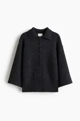 Saco de punto suave color gris oscuro, con cuello camisero y botones frontales. Presenta un diseño de hombros caídos y mangas holgadas que terminan por debajo del codo.