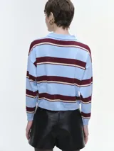 Buzo tejido de punto a rayas horizontales en tonos marrón, rojo y crema, con cuello polo y cierre frontal de botones. Presenta mangas largas con puños elastizados y un corte holgado.