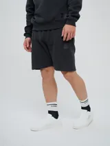 Bermuda de felpa de algodón color celeste, con bolsillos laterales y detalle de costuras verticales al frente. Presenta un parche distintivo de la marca en la pierna izquierda.