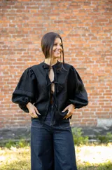 Blusa de lino color negro con mangas abullonadas y cierre frontal mediante lazos ajustables. Presenta un diseño de silueta relajada y escote con abertura.
