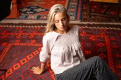 Blusa color rosa pálido de lino con lurex, escote redondo con detalle de nido de abeja, mangas largas con puños elásticos y cierre trasero con botón.