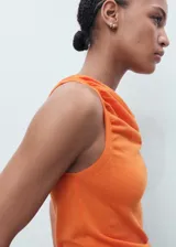 Top de punto fino color naranja, sin mangas, con cuello drapeado y bajo asimétrico.