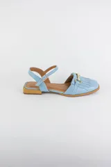 Sandalias de cuero color celeste, con punta cerrada, flecos frontales y detalle de estribo metálico dorado. Tienen tira ajustable al tobillo y suela plana con pequeño taco.