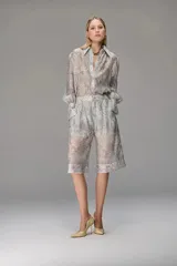 Camisa de organza con textura, de corte holgado, cuello clásico y mangas largas con puños abullonados. Presenta un diseño translúcido con estampado ornamental sutil.