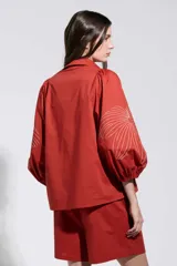 Camisa roja con bordados florales blancos, cuello camisero, cierre frontal oculto y mangas largas abullonadas.