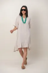 Vestido midi de lino color beige, con mangas cortas, cuello redondo, alforzas verticales en el pecho y detalle de volados en el ruedo.