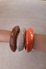 Pulsera rígida de resina con diseño orgánico y acabado brillante, disponible en colores marrón, gris y naranja.