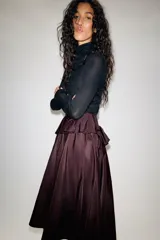 Falda midi asimétrica de color bordó, confeccionada en tejido satinado con volumen. Presenta un diseño con volados en la cintura y cierre de cremallera oculta en la espalda.