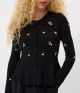 Cardigan negro de punto con bordado floral delicado, mangas largas, escote redondo, cierre frontal con botones y diseño peplum en la cintura.