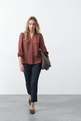 Camisa negra de corte clásico con escote en V, botones frontales y mangas largas con puños. Presenta detalles de recortes calados en la zona de los hombros.