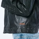Campera de cuero negro con solapas anchas, detalles de tachas en los puños y en el ruedo, y cierre frontal cruzado.