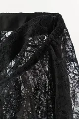Falda midi semitransparente de tiro medio, confeccionada en tejido de encaje negro con detalle de superposición en la cintura y ajuste con lazada. Presenta bajo acabado en ondas y abertura en la espalda.
