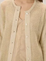 Saco de punto color beige con acabado metalizado, manga larga, cuello redondo y cierre frontal con botones. El diseño combina frente y mangas de tejido abierto con espalda en tela de lino.